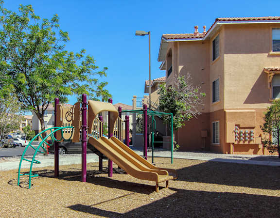 A playground with a slide and a tree in front of a building.